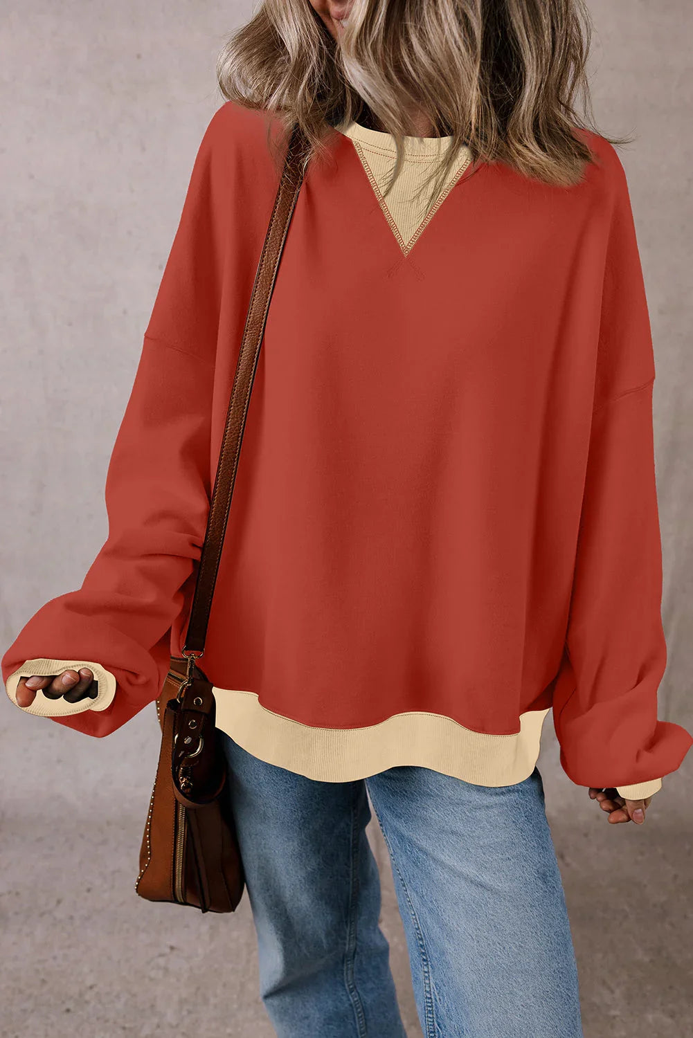 Woman wearing an oversized red pullover sweater with beige trim, blue jeans and brown bag
