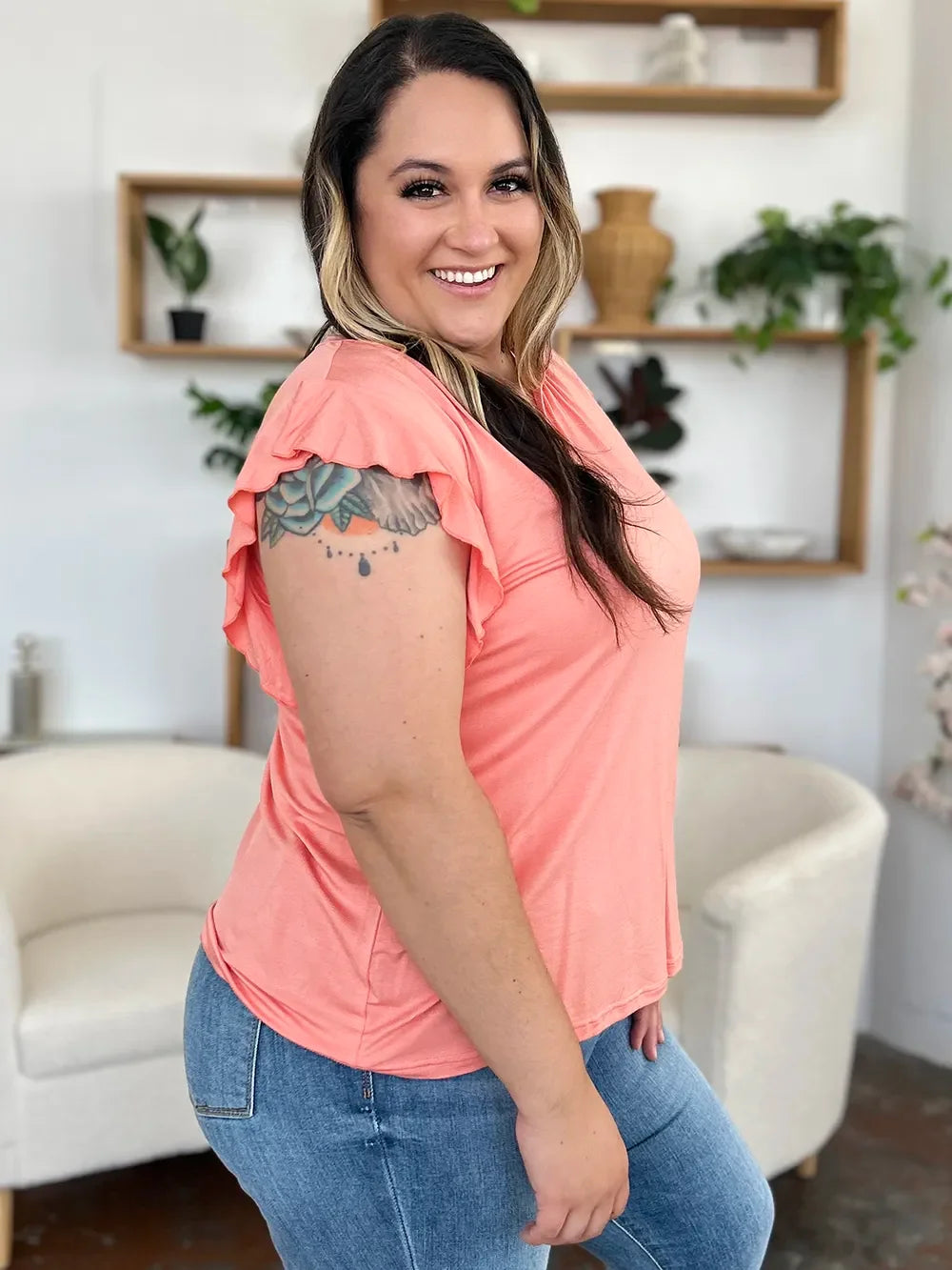 Woman in a peach flutter sleeve top and blue jeans standing in a modern living room