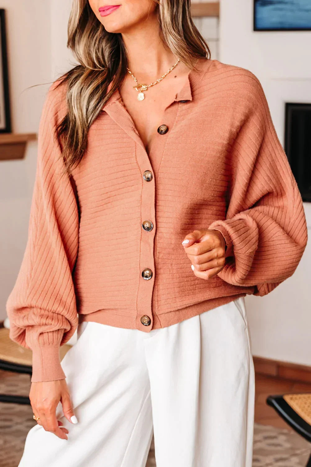 Woman wearing a ribbed, button-up terracotta cardigan with balloon sleeves and white pants
