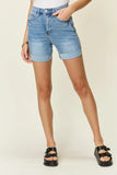 Woman wearing high-rise denim shorts with rolled cuffs and black sandals