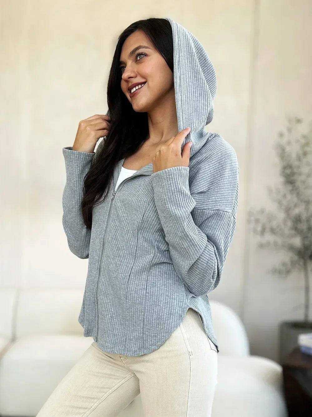 Woman wearing a light gray ribbed zip-up hoodie and cream jeans in a modern living room