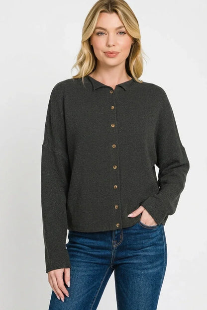 Woman modeling a dark button-up knit cardigan with long sleeves and blue jeans.