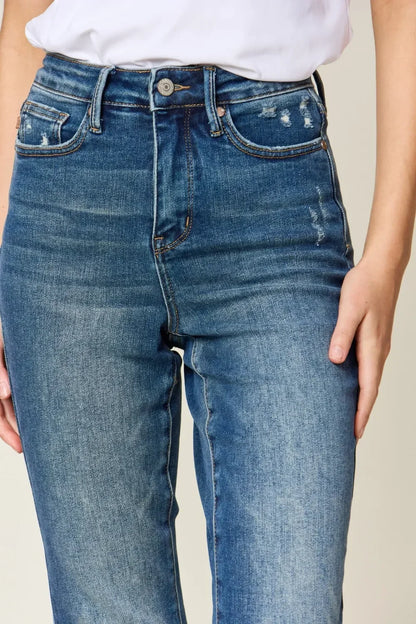 Close-up of high-waisted blue jeans with slight distressing and a relaxed fit, worn with a white top.