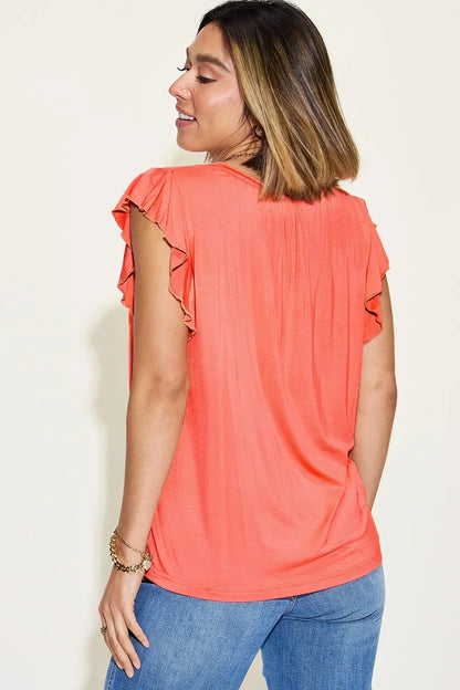 Woman wearing coral flutter sleeve top and blue jeans, shown from the back