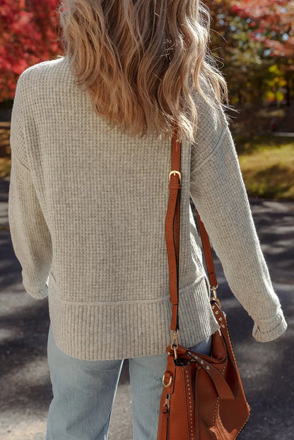 Woman in a textured gray sweater and light-wash jeans carrying a brown leather bag outdoors