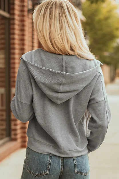 Woman wearing grey hooded sweater and blue jeans, photographed from behind outdoors