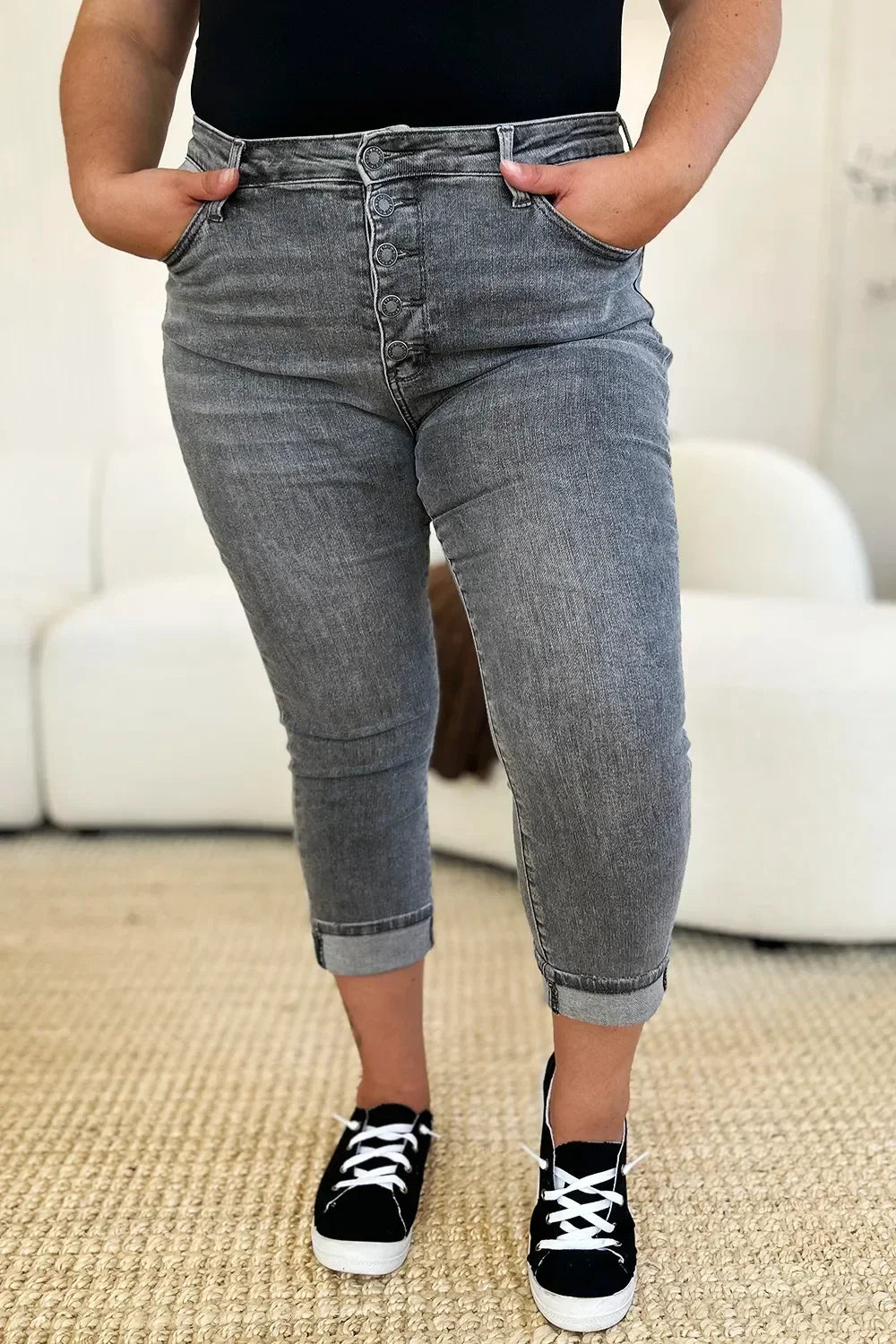 Woman wearing grey high-waisted button fly jeans with cuffed ankles and black sneakers