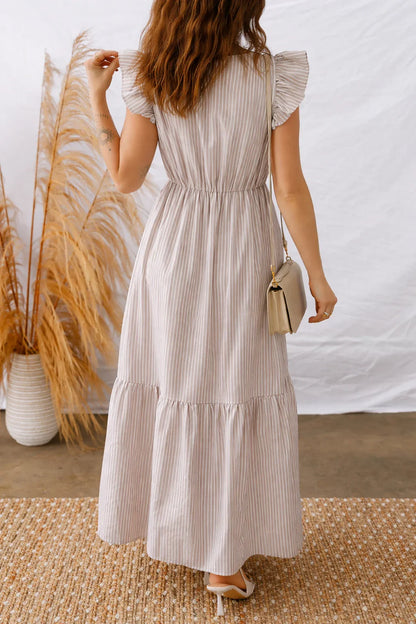 Woman wearing a light striped maxi dress with flutter sleeves, holding a beige purse