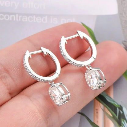 Silver hoop earrings with cubic zirconia dangle, showcased on a hand for detail.