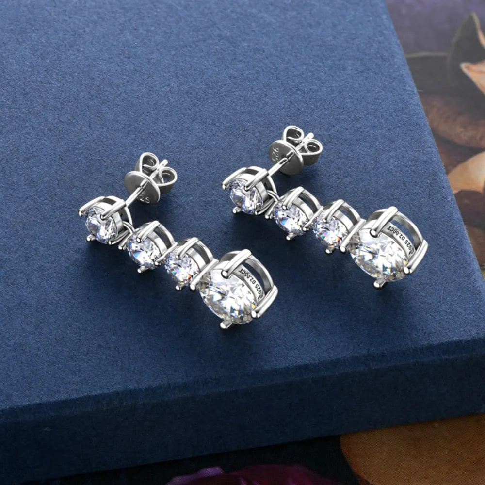 Silver drop earrings with three round clear gemstones on blue textured background