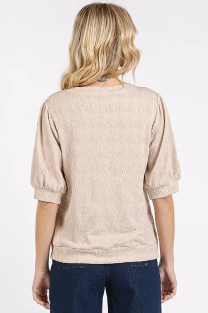 Back view of woman in textured beige blouse with puff sleeves and dark blue jeans.