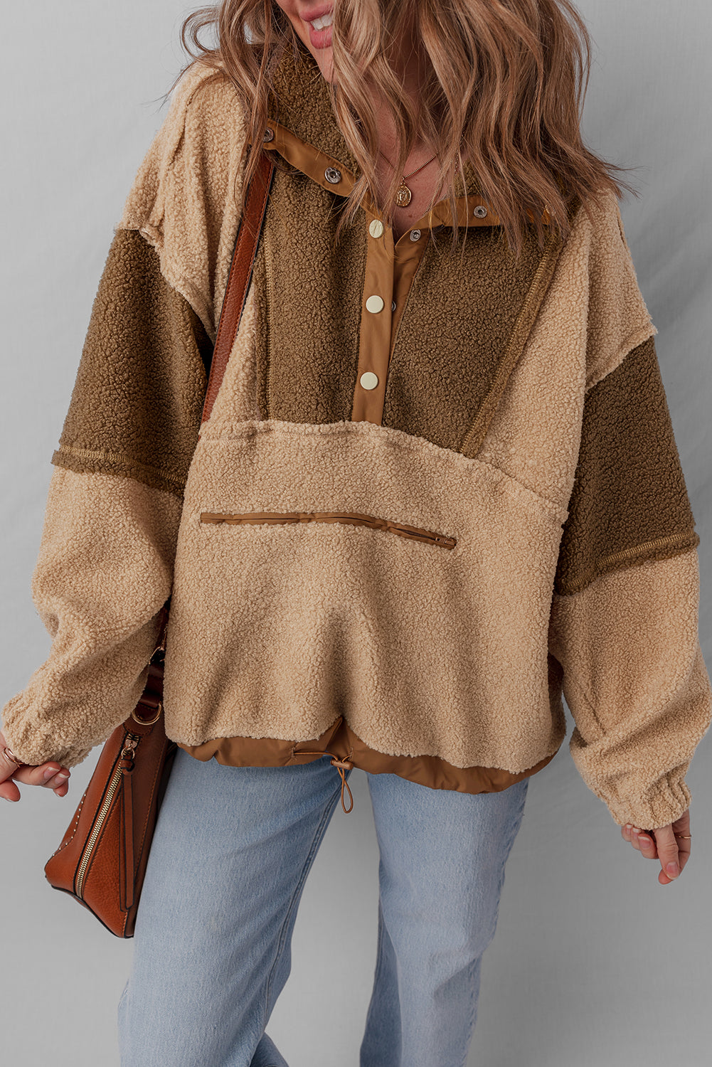 Woman in a beige and brown sherpa pullover with snap buttons and light wash jeans