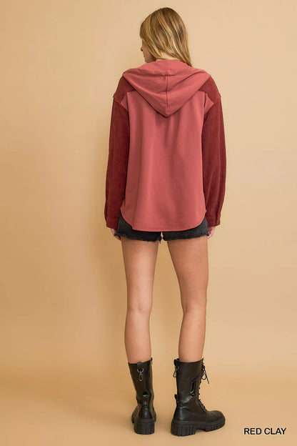 Woman in red clay hooded sweatshirt, black shorts, and black combat boots, back view.