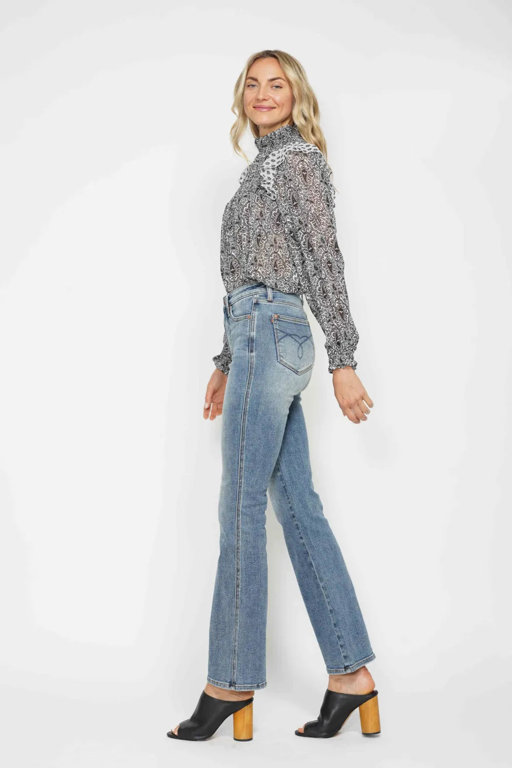 Woman in high neck paisley blouse, straight-leg blue jeans, and black block heel mules