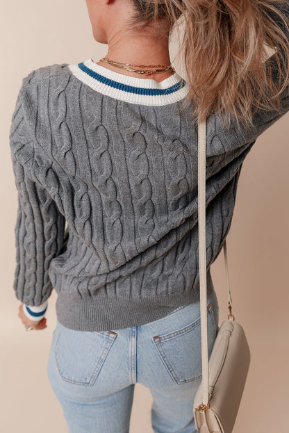 Person wearing a gray cable knit sweater with a blurred background
