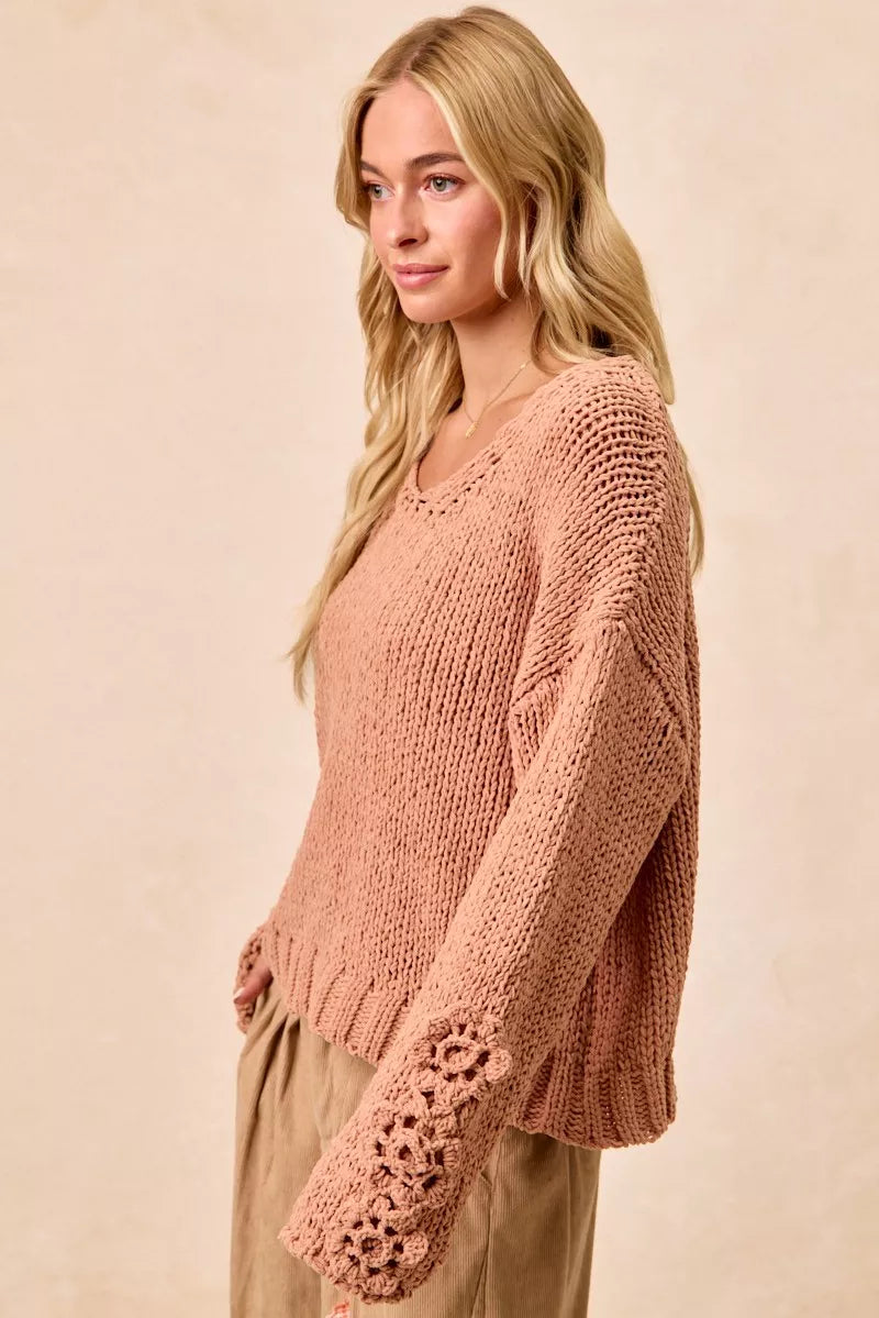 Woman wearing a relaxed fit blush pink knit sweater with floral crochet sleeve detail.