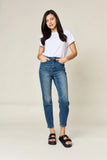 Woman in white t-shirt, high-waisted jeans, and black sandals on plain background