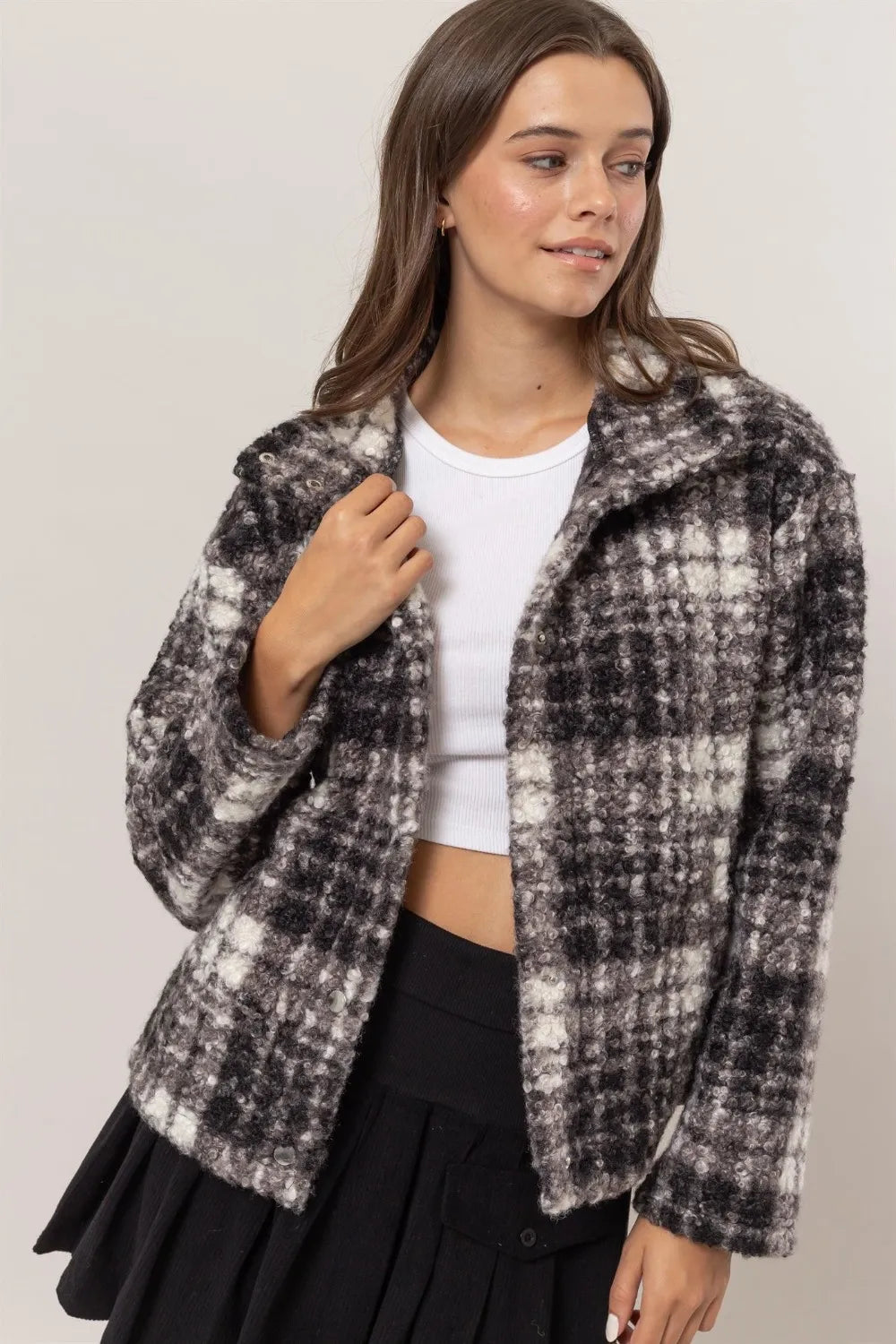 Woman wearing a cropped plaid boucle jacket, white ribbed top, and black pleated skirt