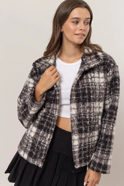 Woman wearing a cropped plaid boucle jacket, white ribbed top, and black pleated skirt