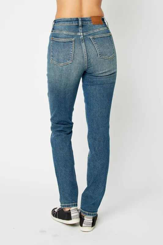 Back view of woman wearing high-waisted straight-leg blue jeans and casual sneakers.