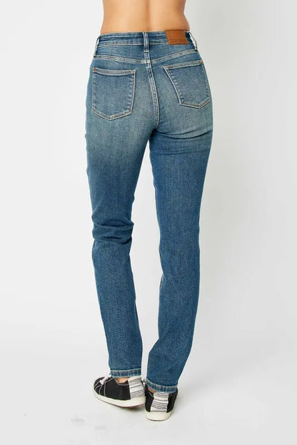 Back view of woman wearing high-waisted straight-leg blue jeans and casual sneakers.