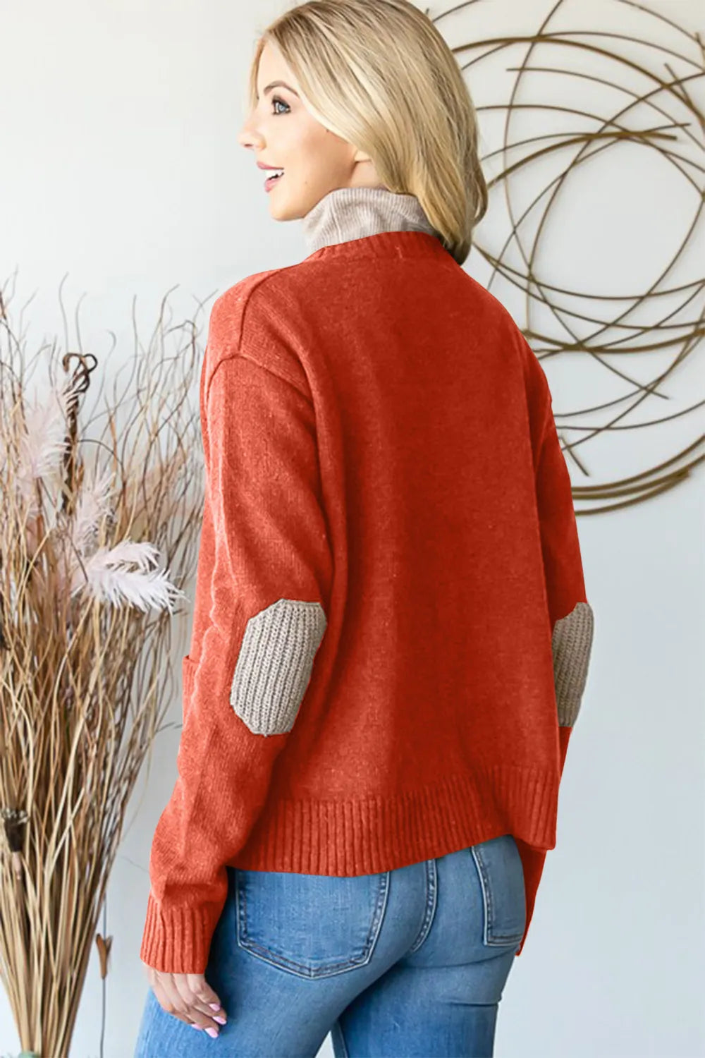 Woman in cozy red sweater with tan elbow patches and blue jeans, modern home decor background