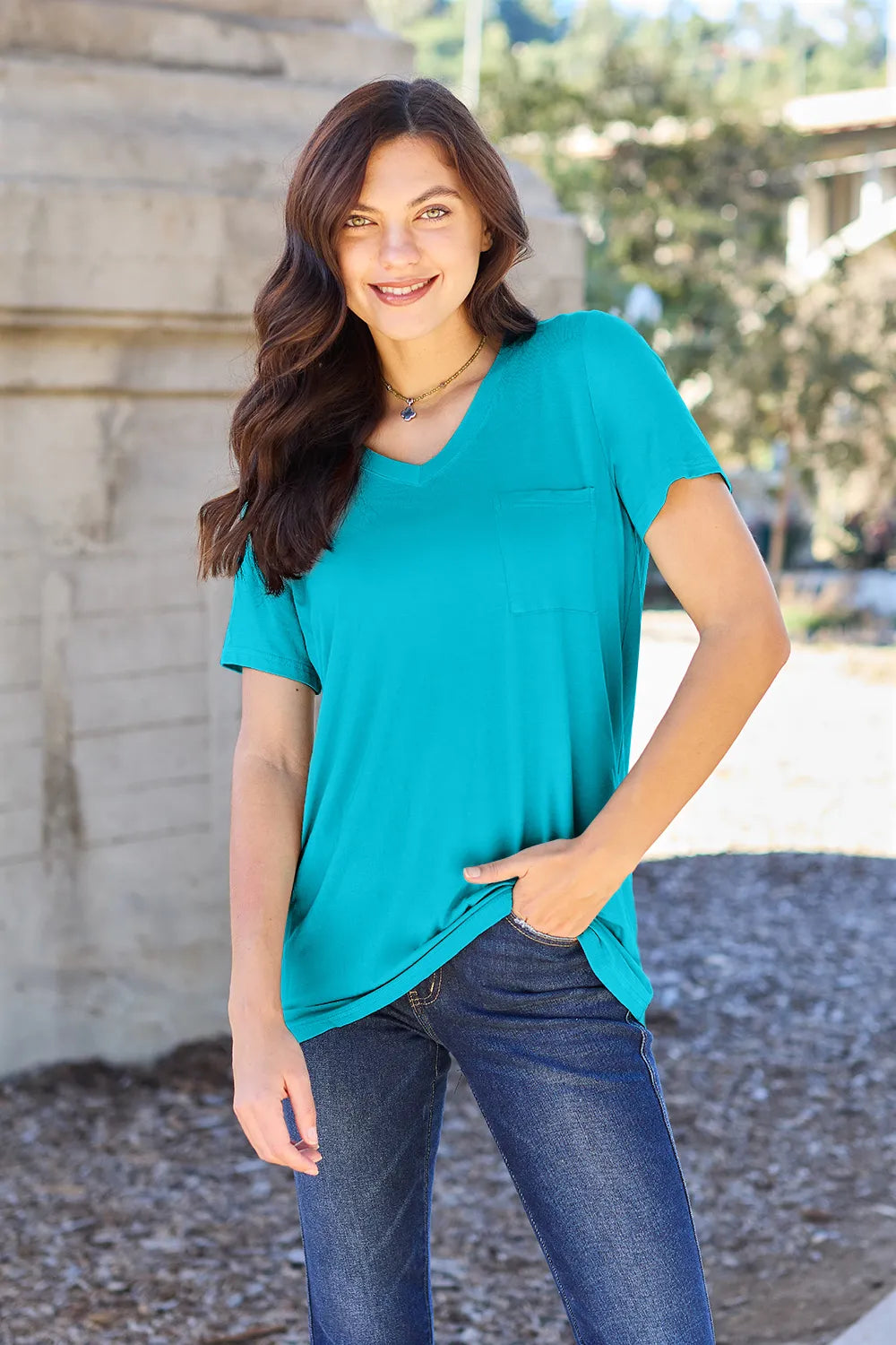 Woman wearing a turquoise short sleeve V-neck pocket top and blue jeans outdoors