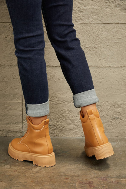 Tan platform lace-up boots styled with cuffed dark denim jeans against a neutral wall.