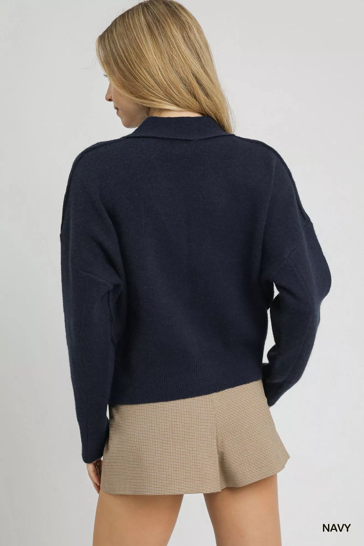 Woman wearing navy sweater and beige plaid mini skirt, back view, minimal background
