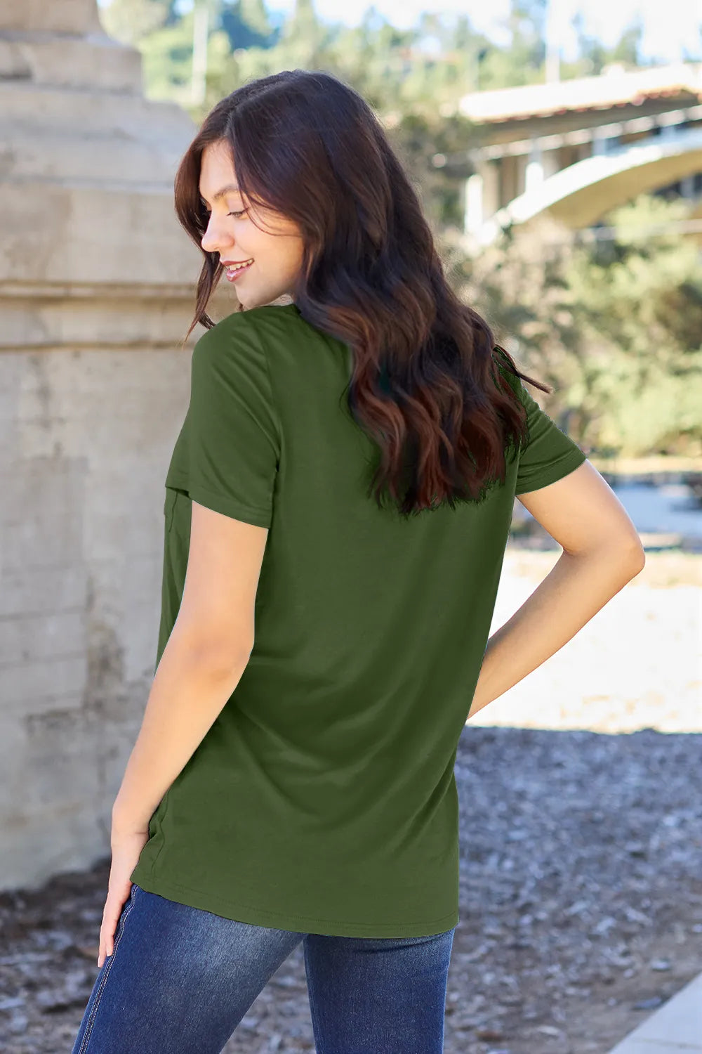 Woman wearing an olive green short sleeve top and blue jeans outdoors