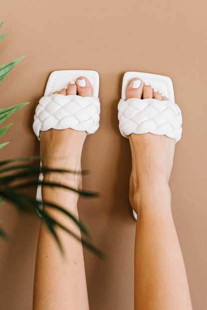 Woman wearing white braided slide sandals with square toes, neutral background, casual fashion
