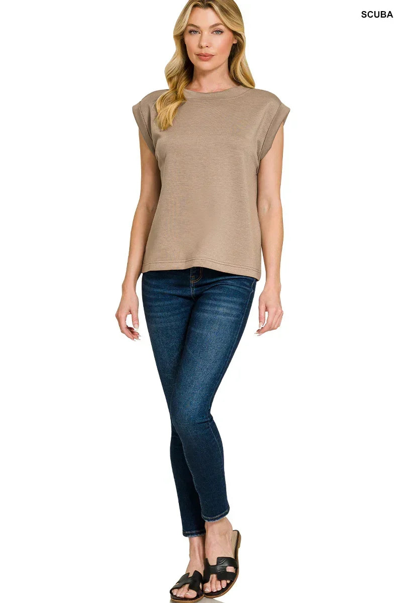 Woman wearing taupe cap sleeve top, dark skinny jeans, and black sandals, standing.