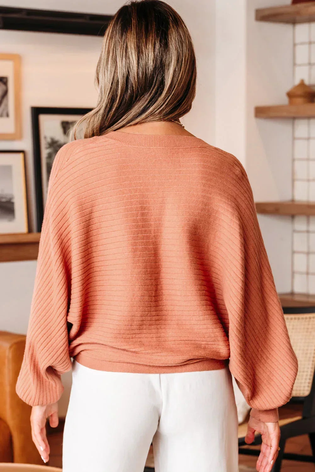 Woman wearing a ribbed, relaxed-fit rust sweater and white pants in a modern living space
