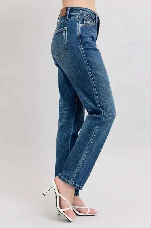 Straight leg blue jeans styled with white heeled sandals on a neutral background
