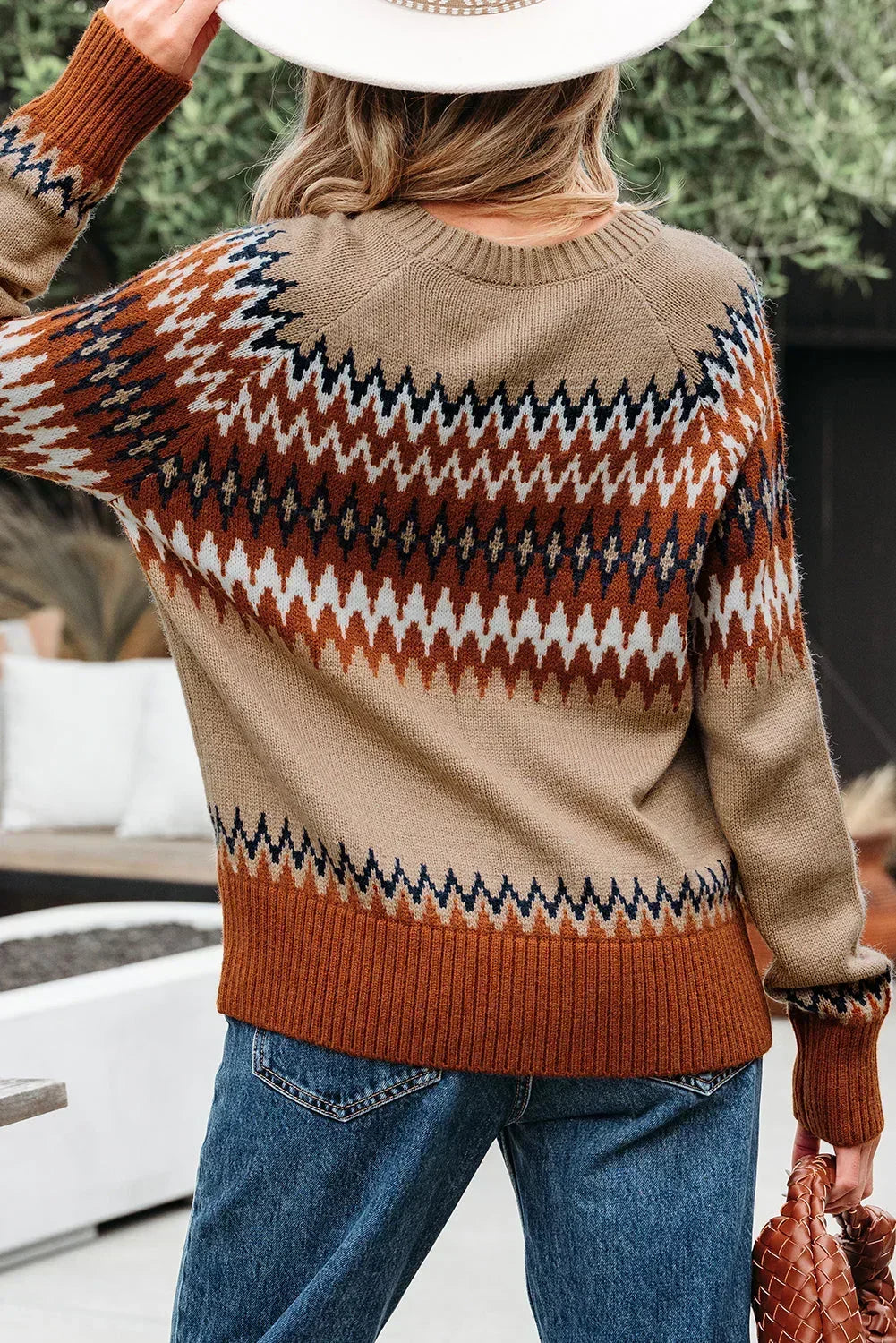 Woman wearing a brown and beige patterned knit sweater with blue jeans outdoors
