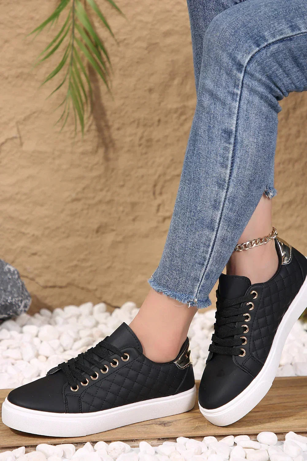 Woman wearing blue skinny jeans and black quilted sneakers with white soles, standing on pebbles