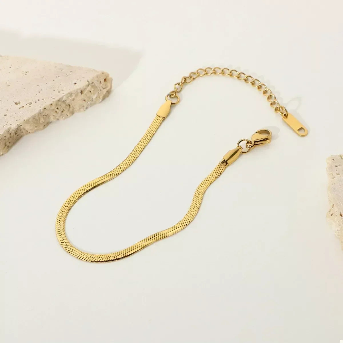 Gold herringbone chain bracelet with adjustable clasp on a minimalist neutral background