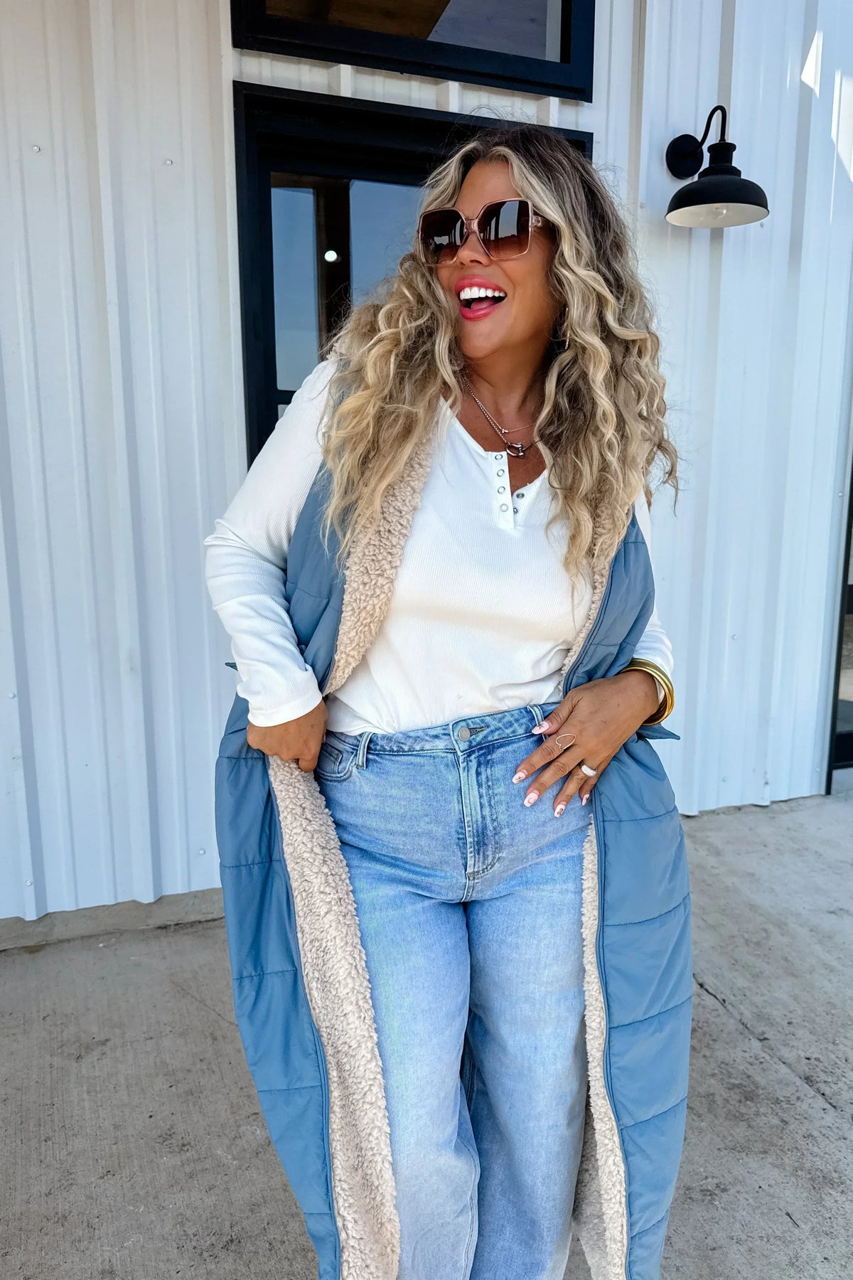 Woman in casual outfit with blue sherpa-lined vest, white henley top, and light wash jeans