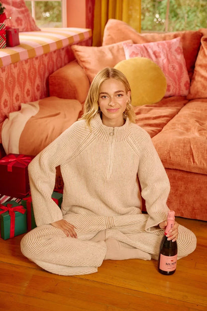 Woman in a cream ribbed knit lounge set sitting by peach sofa with wrapped gifts and rosé bottle