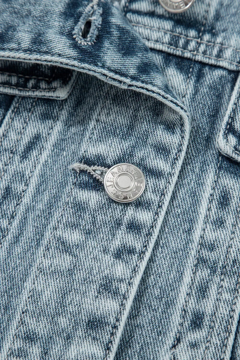 Close-up of light wash denim jacket with silver button and textured stitching detail