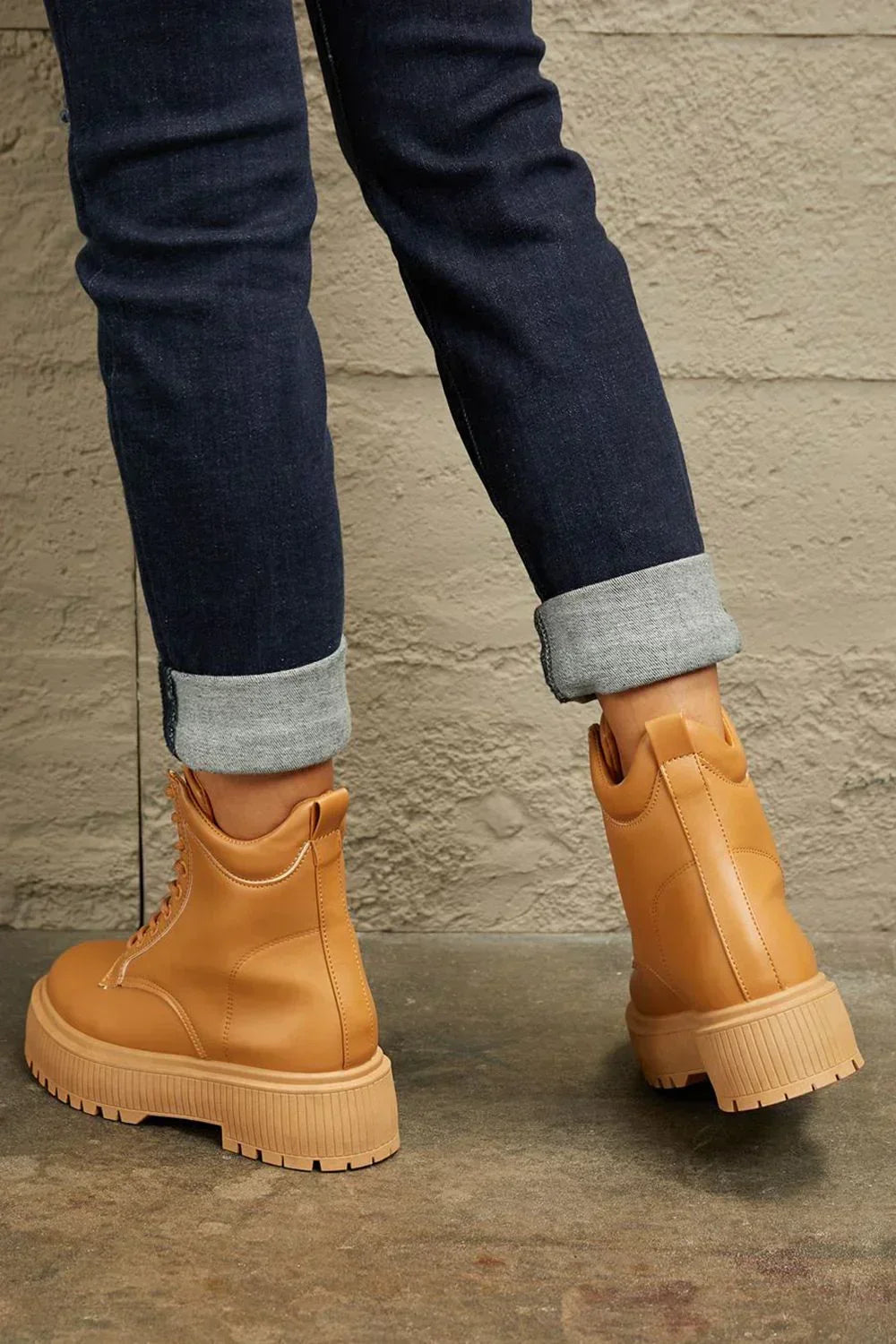 Tan lace-up platform boots styled with cuffed dark wash jeans against a textured wall