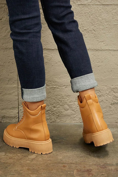 Tan lace-up platform boots styled with cuffed dark wash jeans against a textured wall
