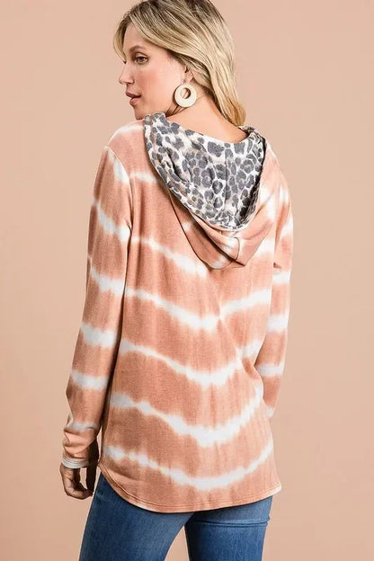 Woman wearing a brown and white tie-dye hoodie with leopard print hood lining, blue jeans