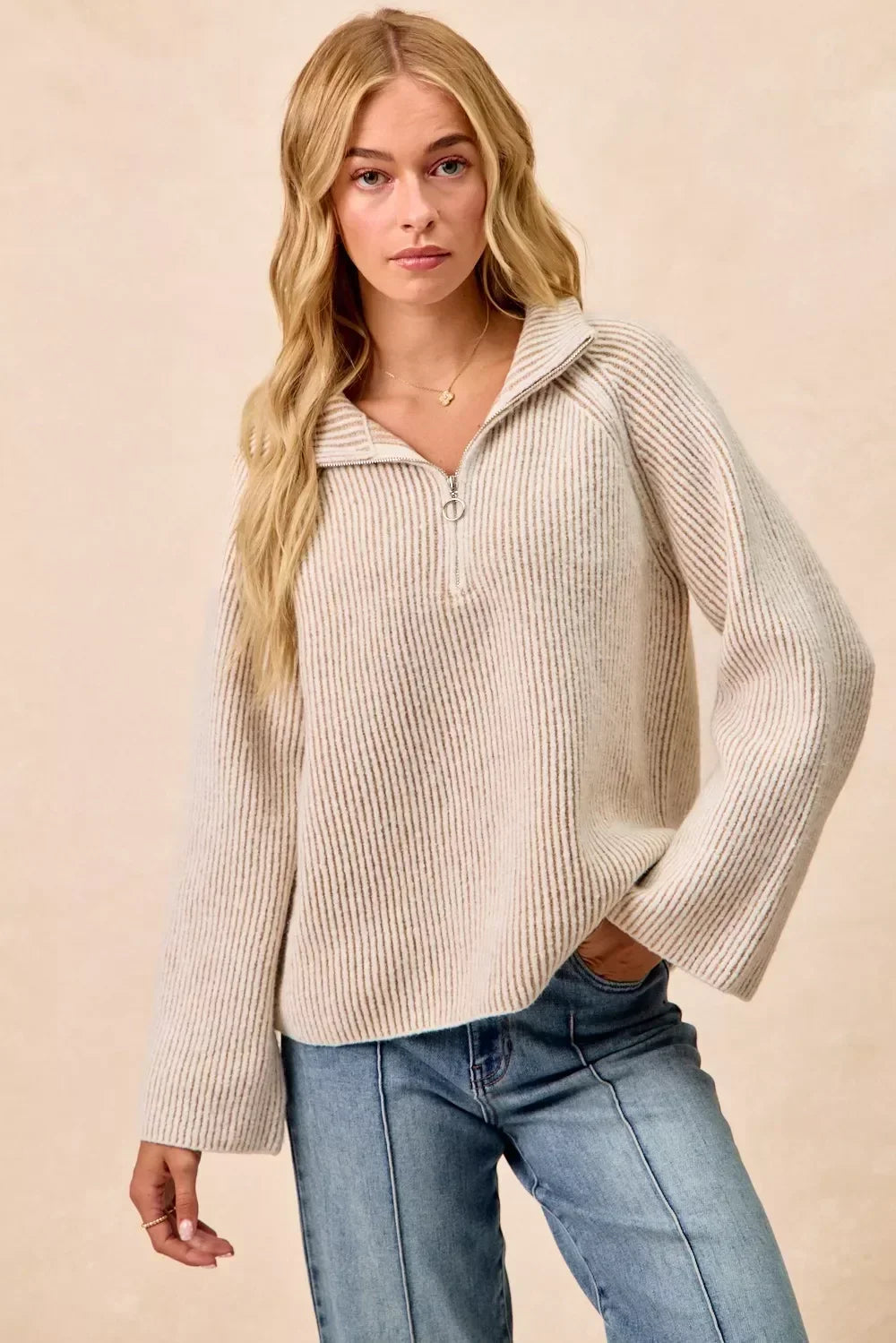 Woman wearing a beige ribbed knit half-zip sweater with relaxed fit and blue jeans.