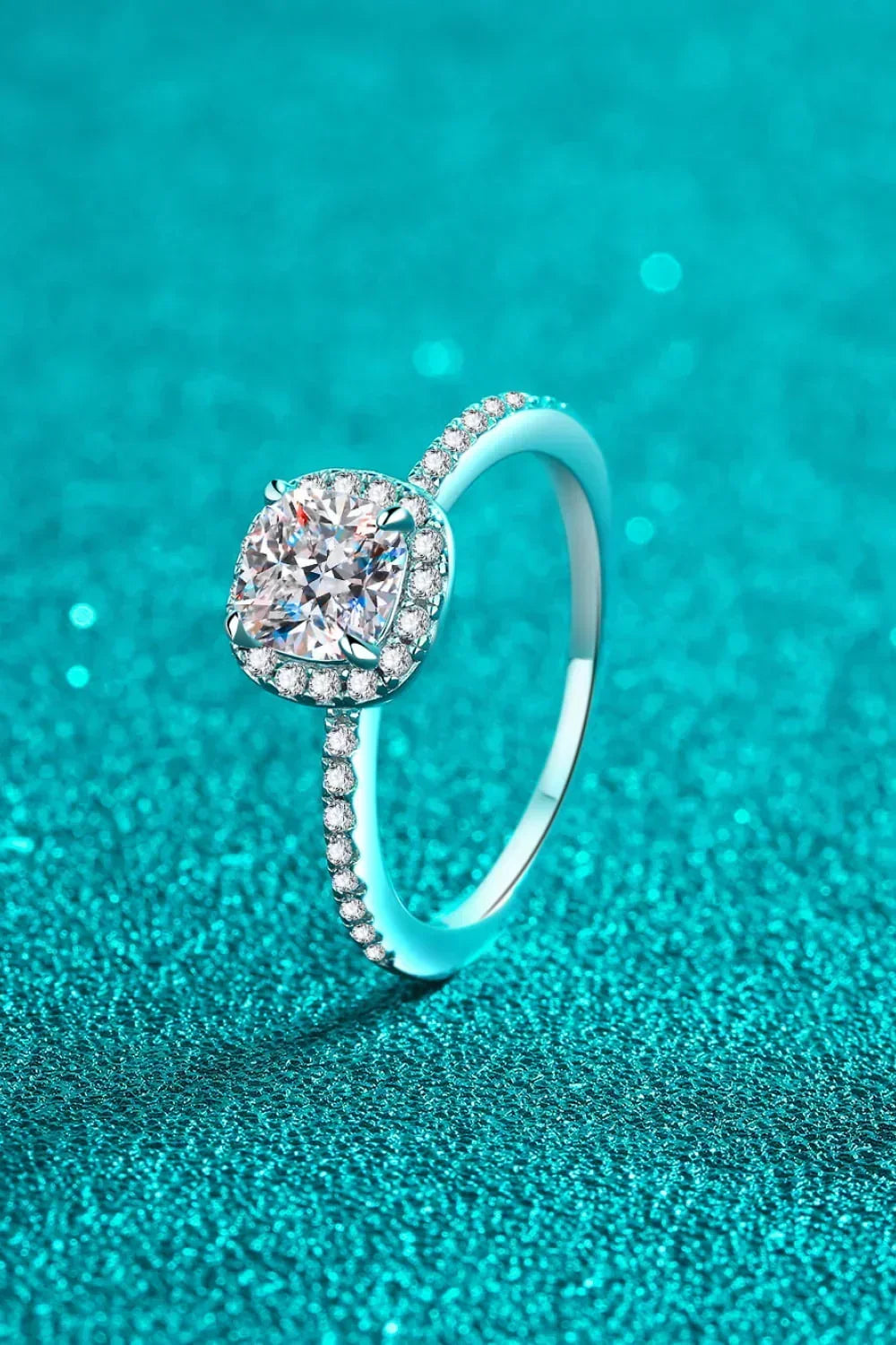 Cushion-cut diamond engagement ring with pavé band on sparkling turquoise background