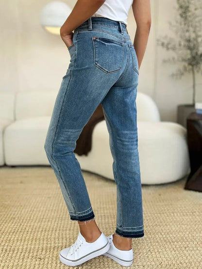 Woman wearing high-waisted straight-leg blue jeans with raw hems and white sneakers indoors