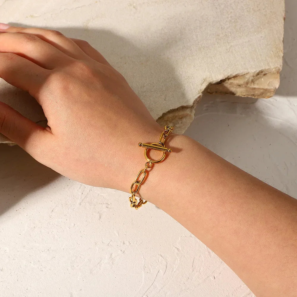 Woman's hand wearing gold chain link bracelet with toggle clasp on textured surface