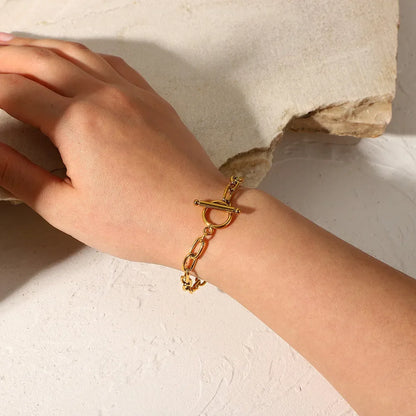 Woman's hand wearing gold chain link bracelet with toggle clasp on textured surface