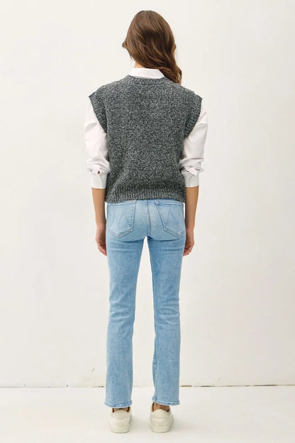 Woman wearing grey sweater vest, white shirt, light blue jeans, and white shoes, back view