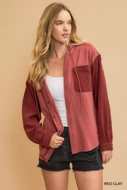 Woman wearing relaxed red clay button-up shirt with textured sleeves and black denim shorts.